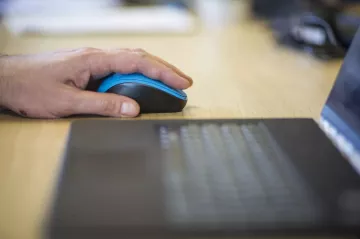 hand holding a mouse next to a computer