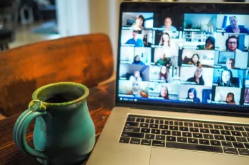 Photo of a laptop showing a webinar, next to a mug