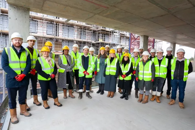 A group of people with high vis and safety equipment on standing in an empty building site