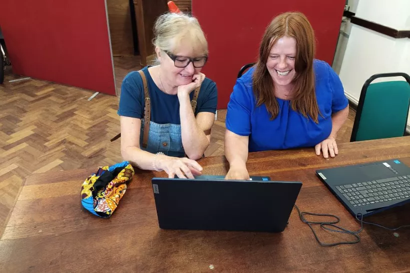 Two women sit at a laptop.