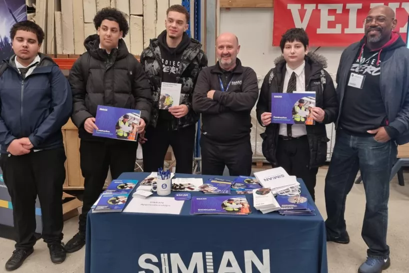 A group of young people attending the 'meet the employer' event, standing behind a table that says SIMIAN on the front