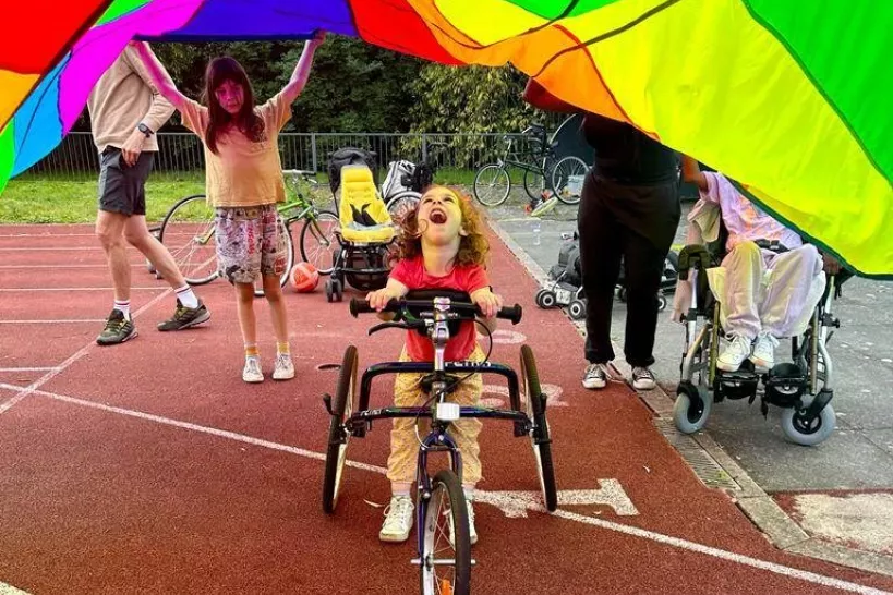 Photo of a young girl using a frame runner on an athletics track, underneath a colourful parachute